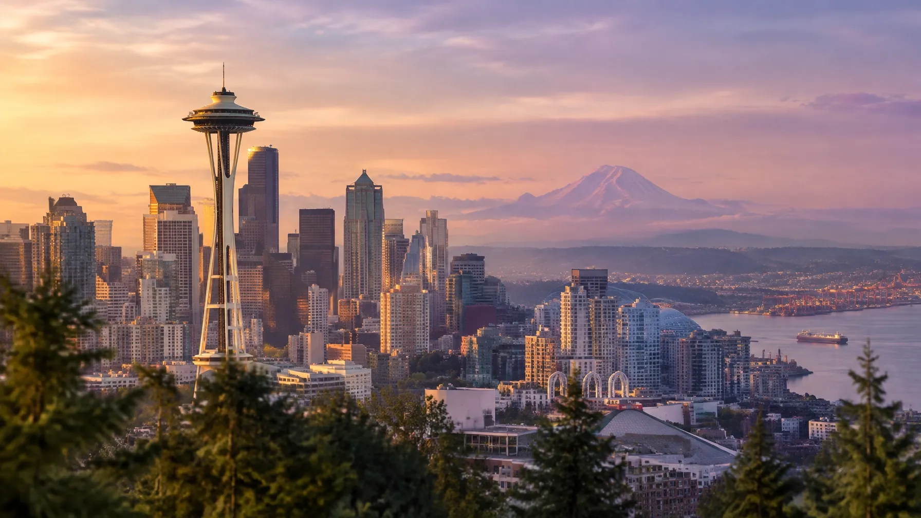 Seattle skyline at golden hour with the Space Needle, Elliott Bay, and Mount Rainier beneath a violet and warm-colored sky