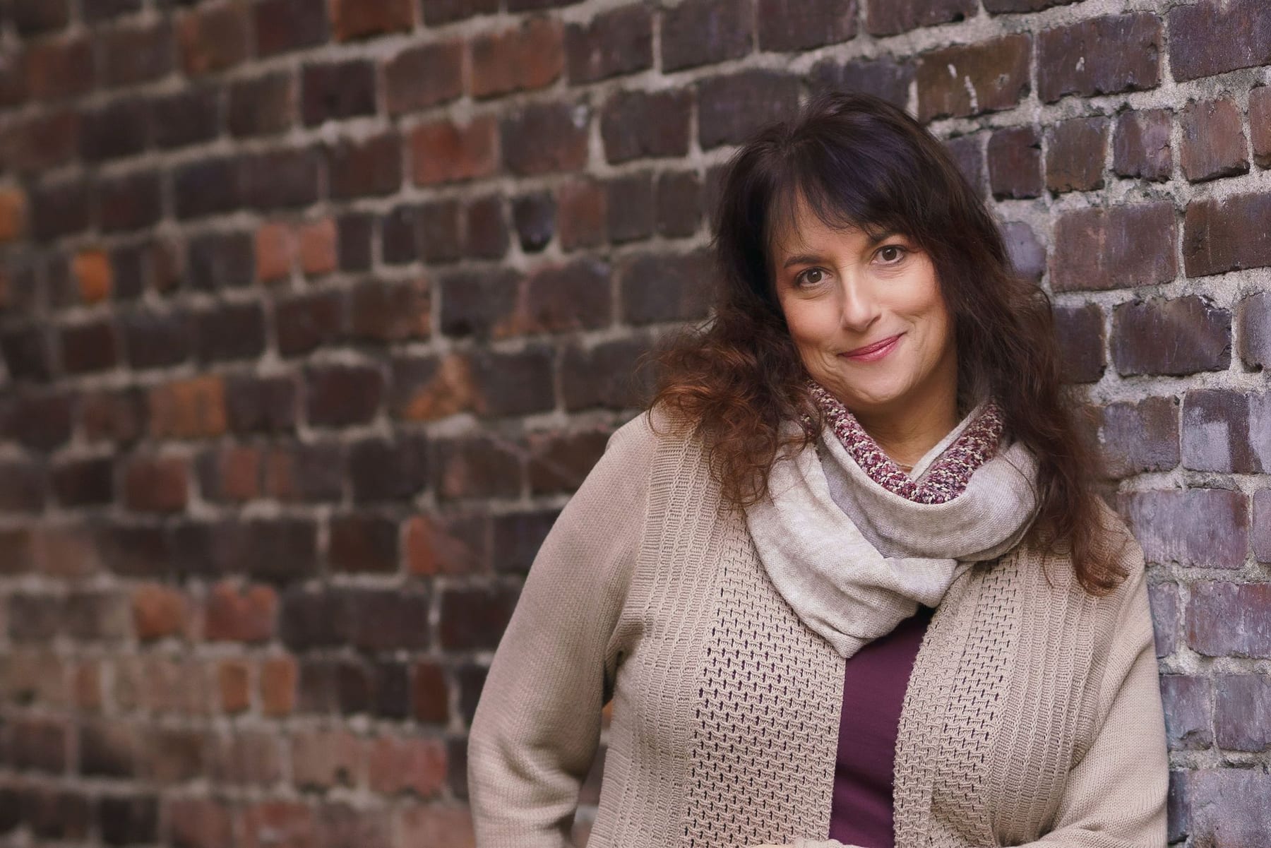 Issy Kleiman, MA, LMFT, looking toward the camera beside a brick wall.