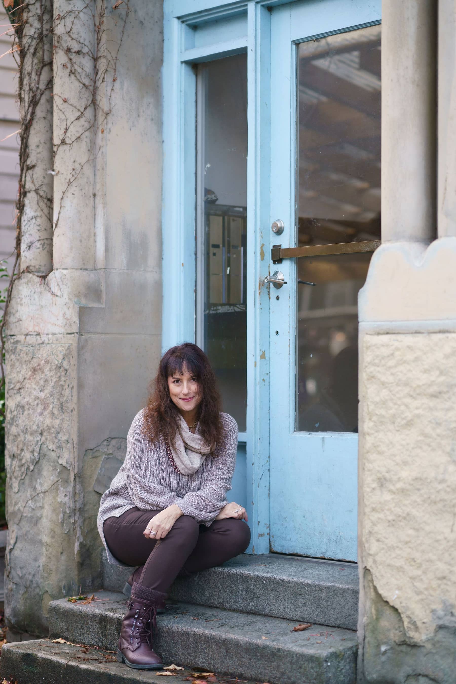 Issy Kleiman, MA, LMFT, seated on the front steps beside a pale blue door.